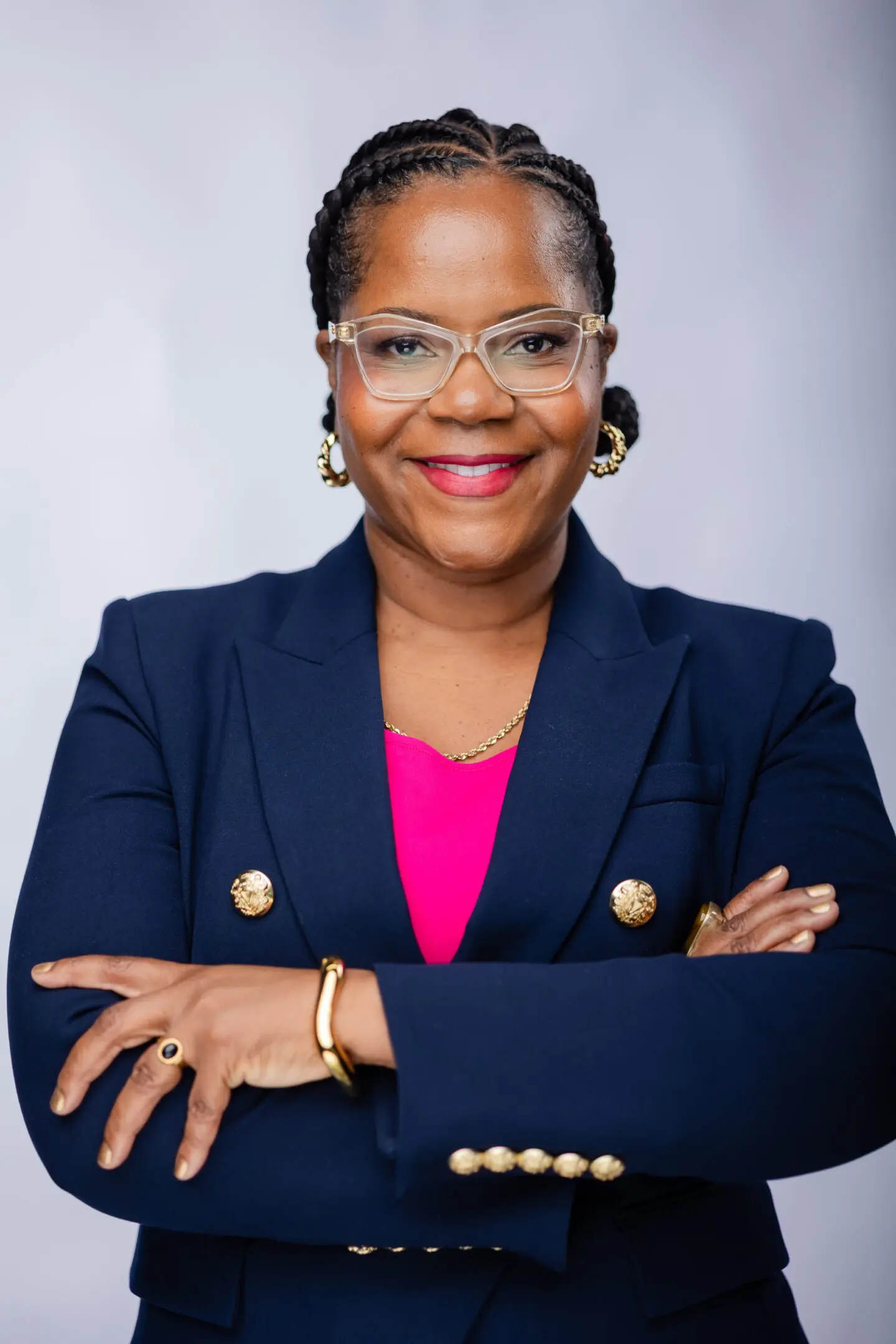 Confident woman in glasses and navy blazer smiling with arms crossed.